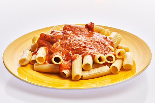Plate of italian rigatoni pasta with tomato sauce over white isolated background
