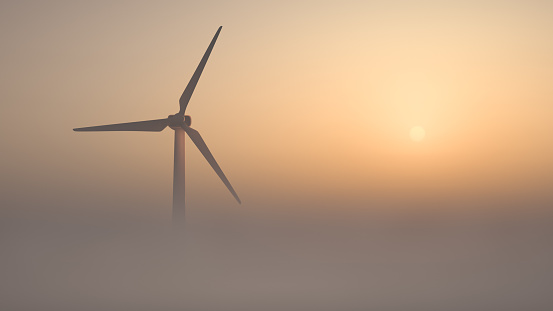 The wind turbine rises out of the mist. The sun is rising in the background. Air view. The theme of clean waste-free energy. Scenic breathtaking view