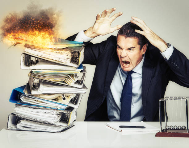 istock Businessman freaks out as fire breaks out on stack of paperwork that threatens to overwhelm him 1396269173