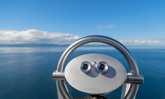 Male hand holding a binocular against the horizon of the sea on the boat on a bright sunny day with a beautiful blue sky