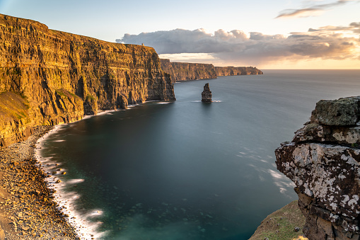 Calm sunset with a view of the cliffs of Moher and rocks in the foreground.