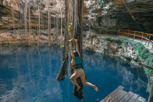 Young Caucasian woman on rope swing in cenote