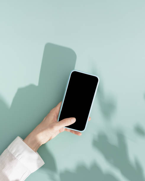 Woman using phone with black blank screen, minimal flat lay on mint blue background. Smartphone mock up. Digital online summer lifestyle composition with leaves shadows and sunlight