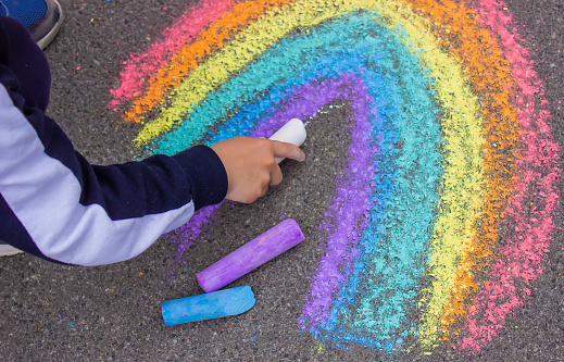 Closeup of a two year old boy playing with sidewalk chalk on pavement.