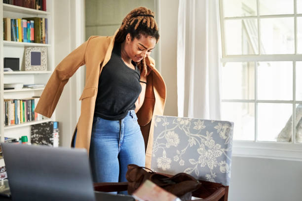 African woman putting on long coat Beautiful young african woman wearing long coat while standing at home trying on stock pictures, royalty-free photos & images