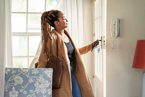 Attractive young african woman wearing long coat with purse opening the door and leaving her home