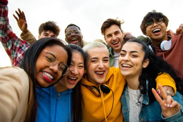 Group of multiracial teen college friends having fun outdoors. Happy people taking selfie. Gen z, friendship and technology concept.