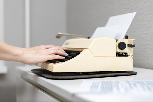 a woman's hand presses a finger on the buttons of an old typewriter