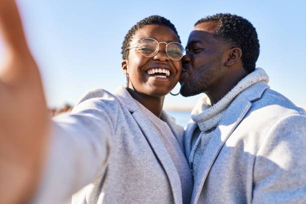 un couple d’hommes et de femmes debout ensemble fait un selfie près de la caméra au bord de la mer - couple black american culture kissing photos et images de collection