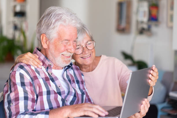 istock Joyful beautiful senior couple smiling at home browsing together on laptop. Active elderly Caucasian couple enjoying technology and social 1396285746