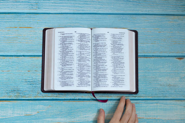 Open Holy Bible Book with hand isolated on a light blue wooden table. Top view from above. Scripture gospel study, relationship with God Jesus Christ Christian biblical concept. Flat lay.