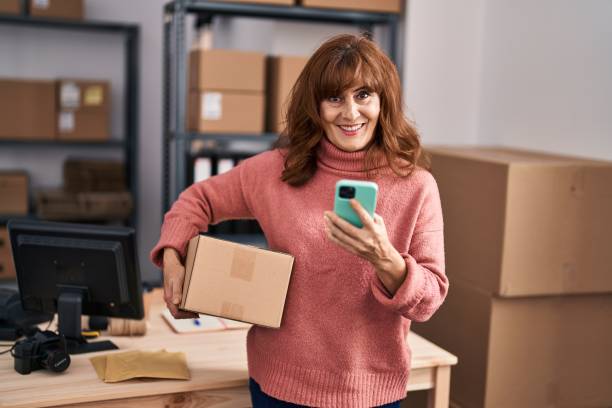 istock Middle age woman ecommerce business worker using smartphone holding package at office 1396288341