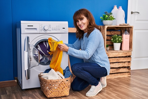 Middle age woman smiling confident washing clothes at laundry room