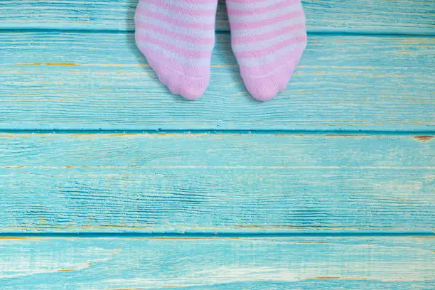 Female feet with lined pink socks isolated on a turquoise blue wooden floor background in vintage style. Copy space. Top view. Overhead shot. The concept of a new beginning and decision making.