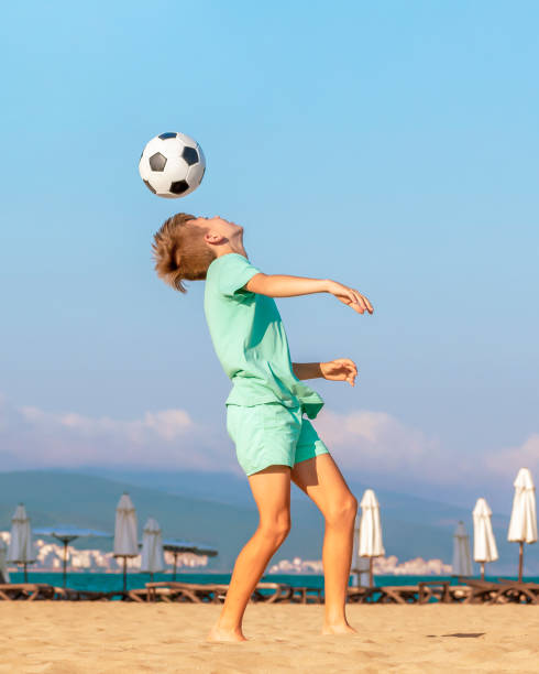 istock Child boy soccer player performs trick by hitting soccer ball with his head while having fun on sea beach during the summer holidays. Kids games and leisure on sandy seashore on vacation 1396288610