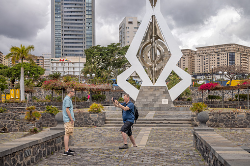 Two tourists taking photographs in front of a modern sculpture by Cesar Manrique (1919-1992) in Santa Cruz which is the main city on the Spanish Canary Island Tenerife