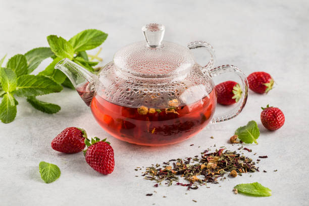 Hot red fruit tea in a glass teapot on a light background decorated fresh mint stock photo