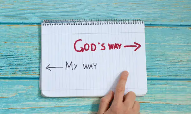 God's way, message quote on a notebook with a hand showing in direction to handwritten arrow isolated on a light blue wooden background. Top view. Follow Jesus Christ's path of eternal life concept.
