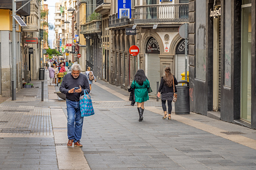 Man in a pedestrian street in causal clothing and with a shopping bag checking his smart phone in Santa Cruz which is the main city on the Spanish Canary Island Tenerife
