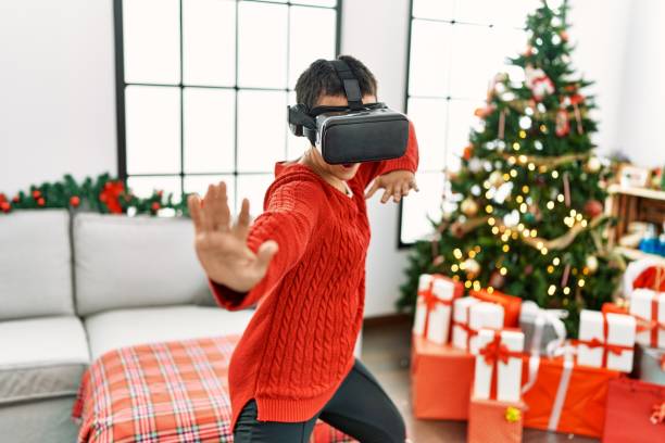 istock Young hispanic woman playing video game using vr glasses standing by christmas tree at home 1396290221