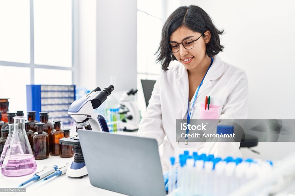 Young latin woman wearing scientist uniform using laptop working at laboratory Latin American and Hispanic Ethnicity Stock Photo