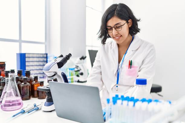 Young latin woman wearing scientist uniform using laptop working at laboratory stock photo
