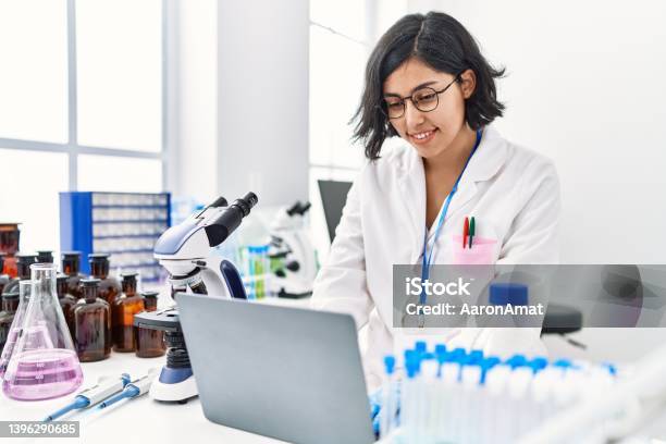 Young Latin Woman Wearing Scientist Uniform Using Laptop Working At Laboratory Stock Photo - Download Image Now