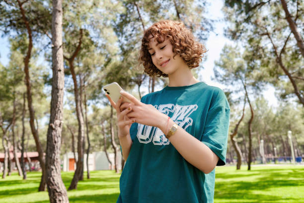 Young redhead woman wearing green tee with smiles looking at the phone. Sportive woman texting or scrolling or watching video on smart phone. stock photo