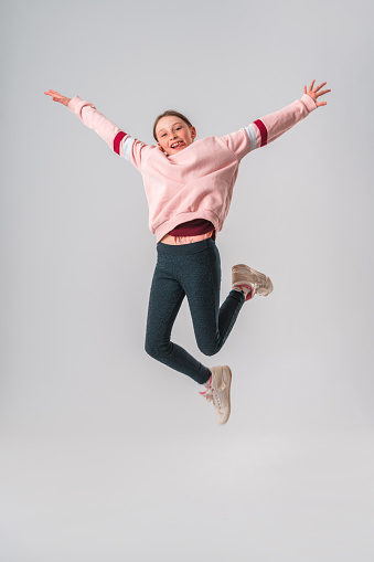 Portrait of a Caucasian teenage girl in the studio. She is jumping in the air with her arms raised. She is looking at the camera. White background.