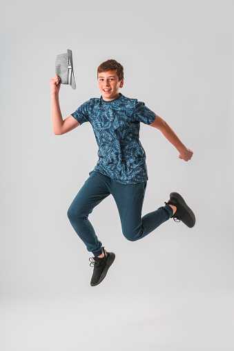Portrait of a Caucasian teenage boy in the studio. He is jumping in the air with his arms raised. He is looking at the camera. White background.
