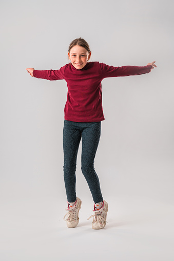 Portrait of a Caucasian teenage girl in the studio. She is standing on her toes and is looking at the camera. White background.