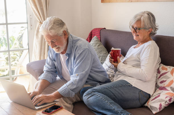 istock Relaxed caucasian senior couple sitting at home on sofa using laptop. Two elderly retirees enjoying tech and social 1396292460