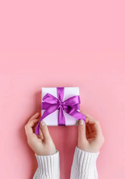 Female Hands in sweater holding gift in white wrapping paper on pink background. St. Valentines Day, Mothers' Day, love, friendship, Birthday, Christmas concept. Cozy, festive, romantic wallpaper