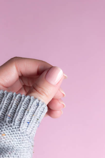 istock Hand in sweater with nude nails on pink background 1396293481