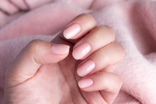 Hand in sweater with nude nails on pink textile background
