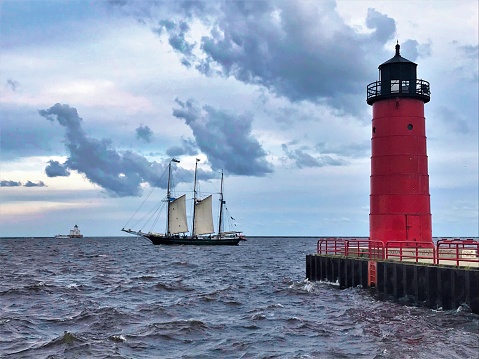 On a cloudy day South of Milwaukee, a replica sailing ship passes between two lighthouses on Lake Michigan.