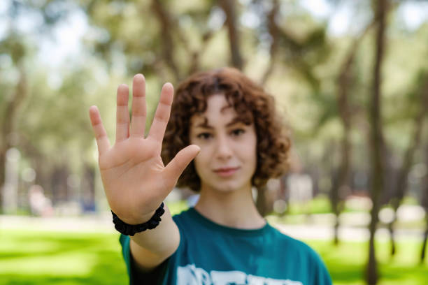 Young redhead woman wearing green tee doing stop sign with palm of the hand. Warning expression with negative and serious gesture on the face. Selective focus on her hand. stock photo