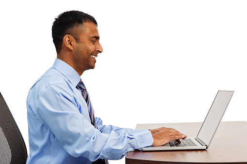 Photo of an Indian business man working with a smile at his desk, reading and writing email; isolated on white.