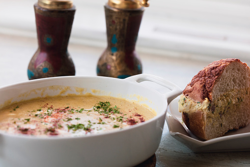 A bowl of homemade cream of chicken soup, accompanied by a  cheese bread stuffed with egg salad.