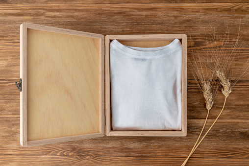 Mock-up of a white T-shirt inside a wooden box on a dark wooden table and some ears of wheat