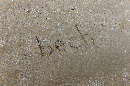 In the sand on the beach, someone has written a message with the word beach, small emoticon, no one can be seen, with copy space