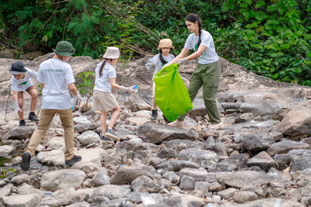 Volunteer Asian and children are collecting plastic bottles that flow through the stream into garbage bags to reduce global warming and environmental pollution. Volunteering and recycling concept. stock photo