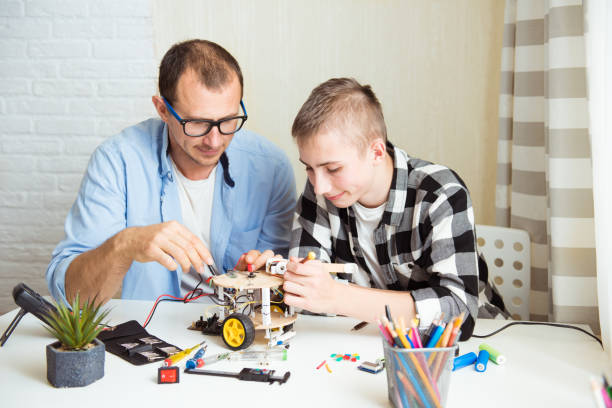 istock Father and son sitting by the white table and building robot at home as a school science project. STEM-education, distance learning, technology concept, hobby idea 1396302099