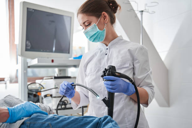 ärztin mit schutzmaske, die während der gastroskopie ein endoskop hält - gastroenterologe stock-fotos und bilder