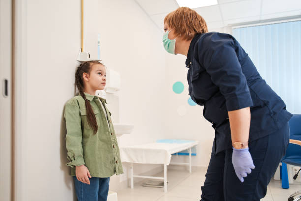 female doctor measuring height of little girl in clinic - tall human height women measuring imagens e fotografias de stock