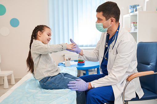 Side view happy little preschool girl giving high five to male doctor at meeting in hospital. Smiling small patient celebrating treatment finish with general practitioner