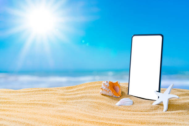 istock Smartphone standing on beach sand with bright sun. Copy space 1396304914