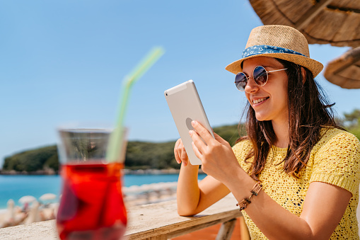 Beautiful young woman working on tablet in a beach café while on a travel destination.