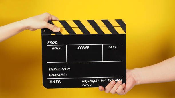 istock Two hands send and hold a Black clapper board or movie slate on yellow background. 1396311017