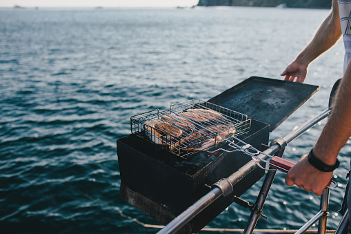 Man grilling fish on yacht with beautiful ocean view.